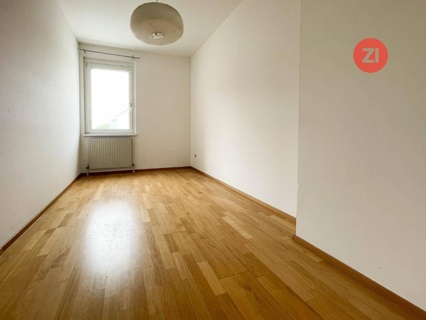Helles Schlafzimmer mit einem Fenster, Holzboden und Deckenleuchte, ideal für Ruhe und Entspannung.