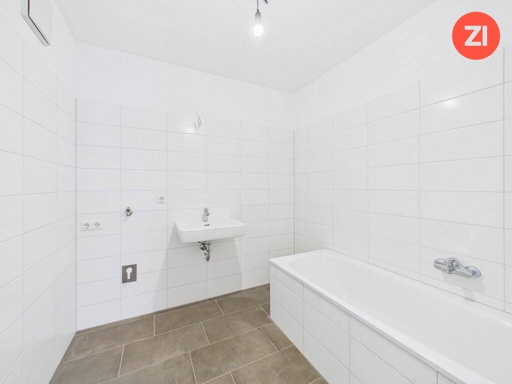 Modern gefliestes Badezimmer mit Badewanne und Waschbecken, bereit für die Endmontage.