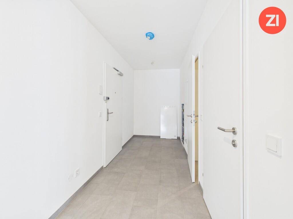 Heller Flur mit grauen Fliesen und weißen Türen, der den Eingangsbereich des Apartments bildet.