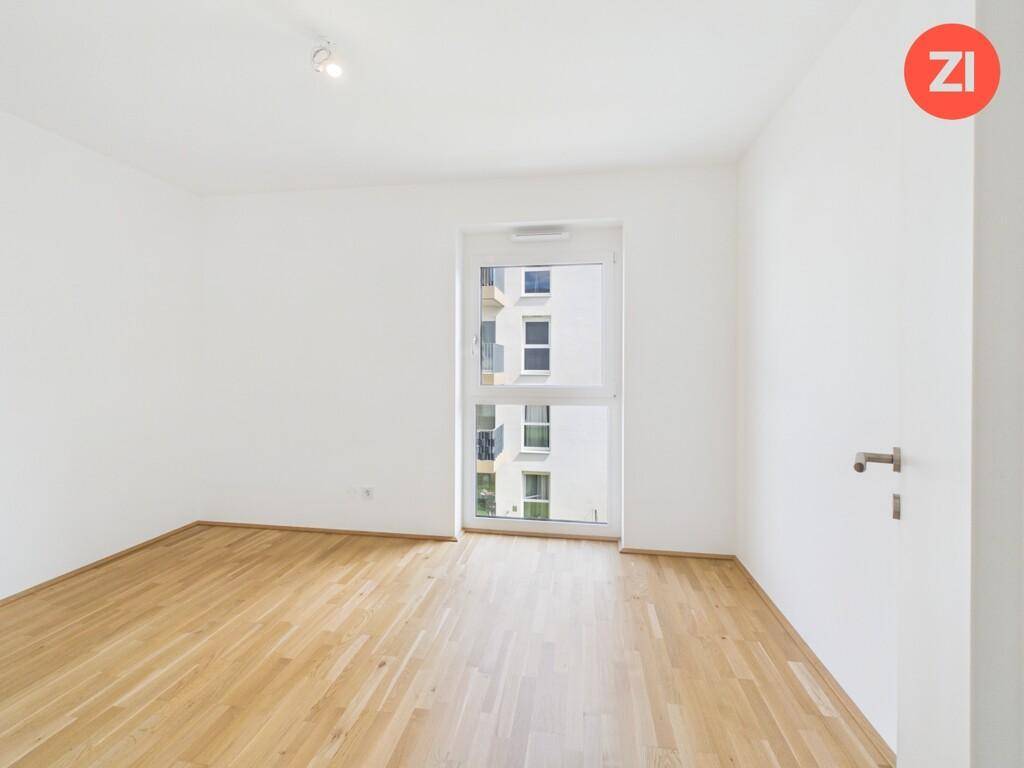 Helles Schlafzimmer mit Holzboden und Fenster mit Blick auf die umliegenden Gebäude.