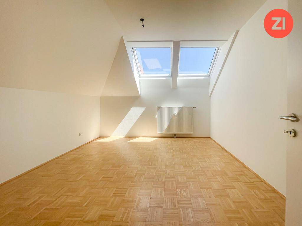 Lichtdurchflutetes Zimmer mit Parkettboden, Dachschrägen und großen Dachfenstern.