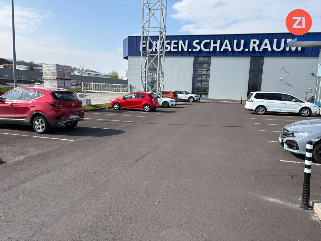 Großer Parkplatz vor einem Geschäftsgebäude unter blauem Himmel, mit mehreren geparkten Autos.