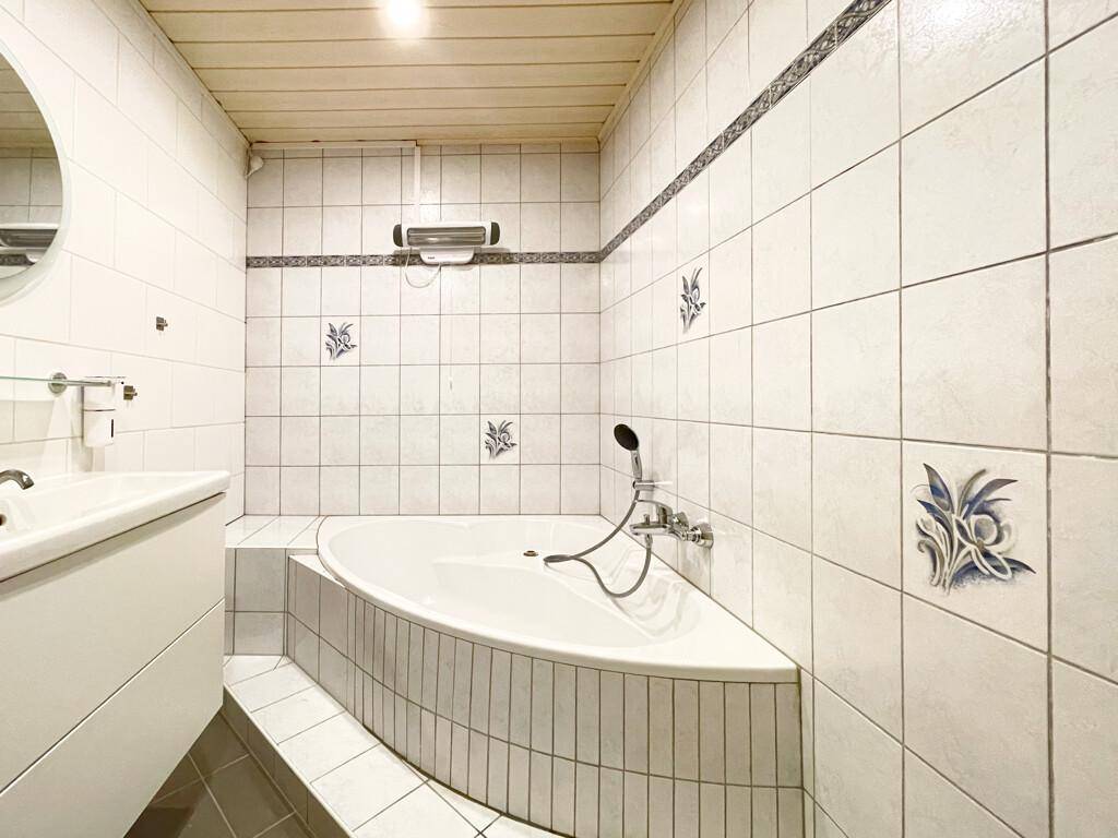 Badezimmer mit Eckbadewanne, weißen Fliesen und Holzdecke für entspannende Momente.