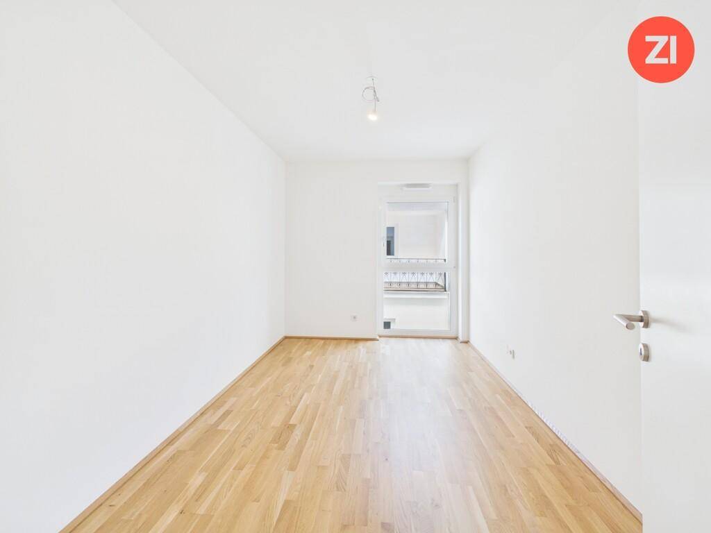 Unmöbliertes Zimmer mit Holzboden und Fenster, das viel Tageslicht in den Raum lässt.