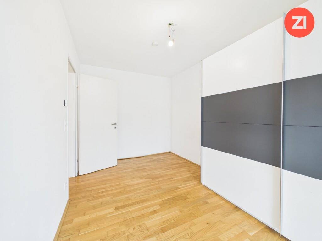 Helles Schlafzimmer mit Parkettboden, weiß gestrichenen Wänden und einem großen Kleiderschrank.