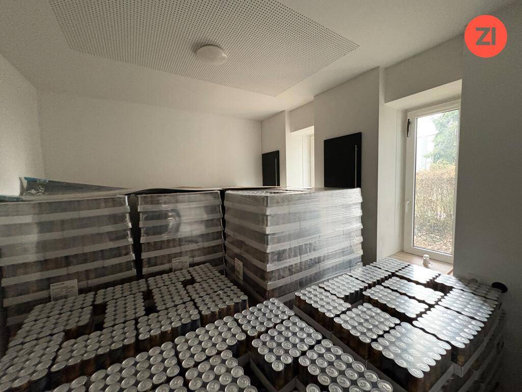 Lagerraum mit hohen Stapeln von Waren und einem Fenster mit Blick ins Grüne.