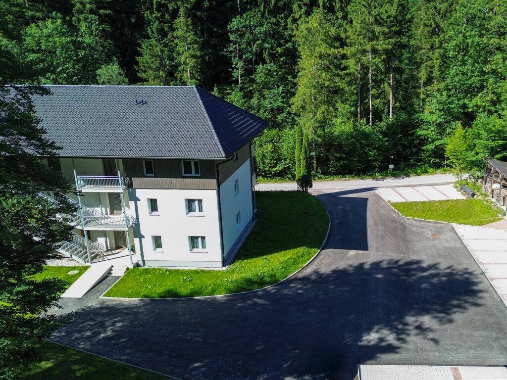 Gebäudeansicht von oben mit Zufahrt und Parkplätzen, umgeben von Wald.