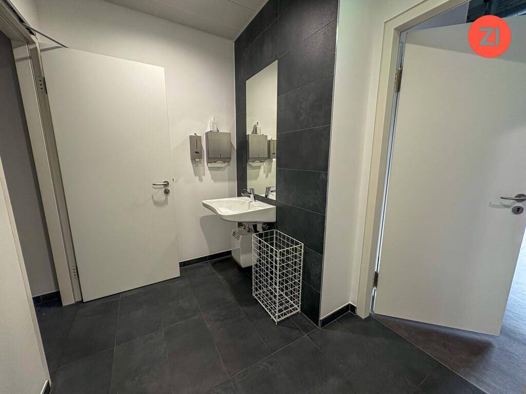 Moderner Toilettenbereich mit Waschbecken, Spiegel und dunklem Fliesenboden.