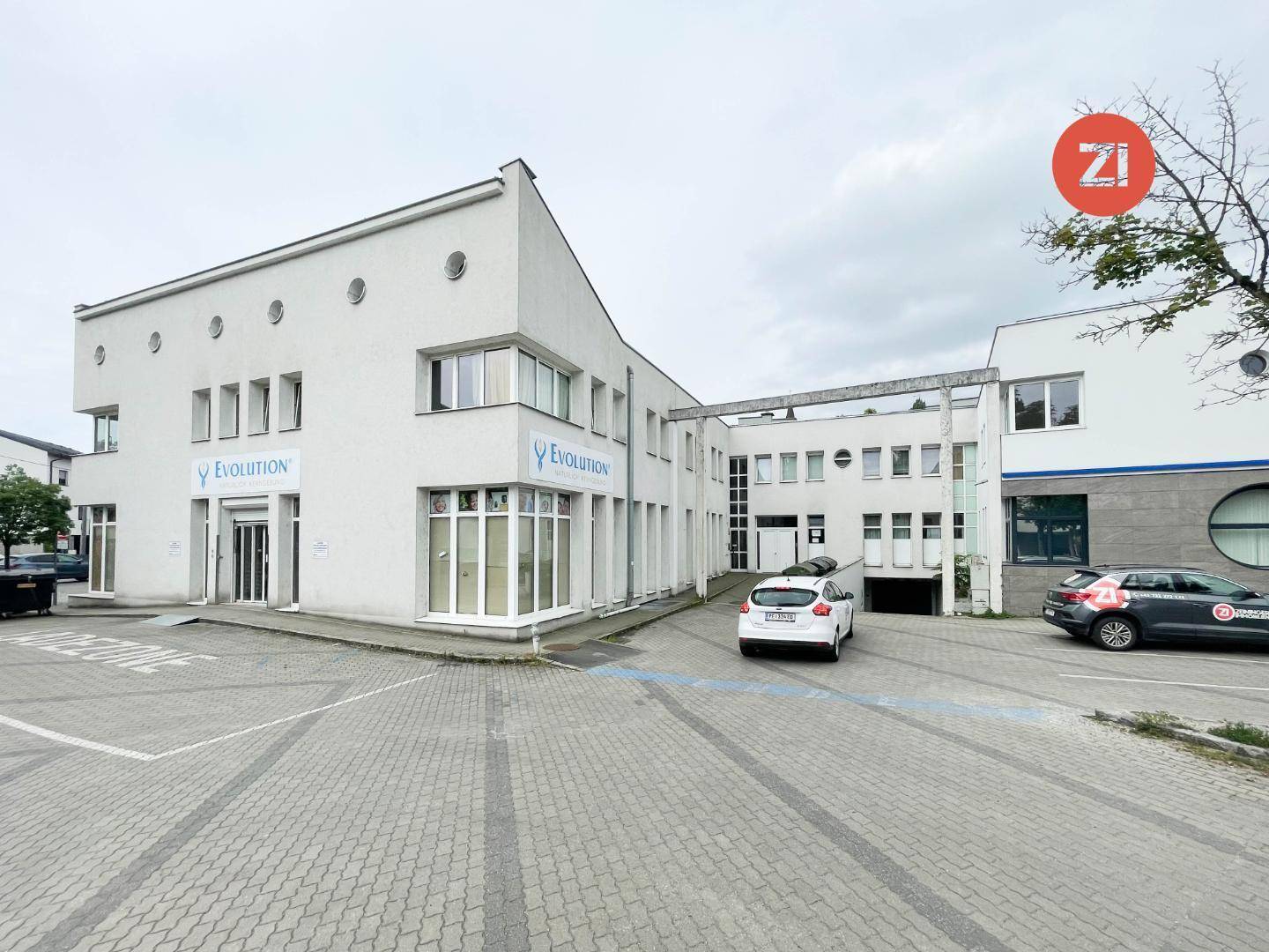 Modernes Geschäftsgebäude mit weißer Fassade, großen Fenstern und ausreichend Parkplätzen.