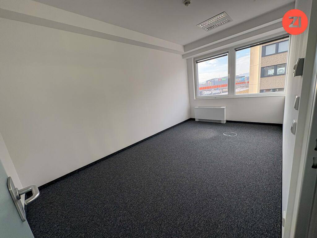 Kleines, helles Büro mit Teppichboden und einem Fenster, das Tageslicht hereinlässt.