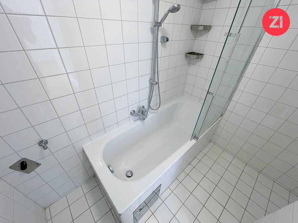 Helles Badezimmer mit weiß gefliesten Wänden und einer Badewanne mit integrierter Dusche.