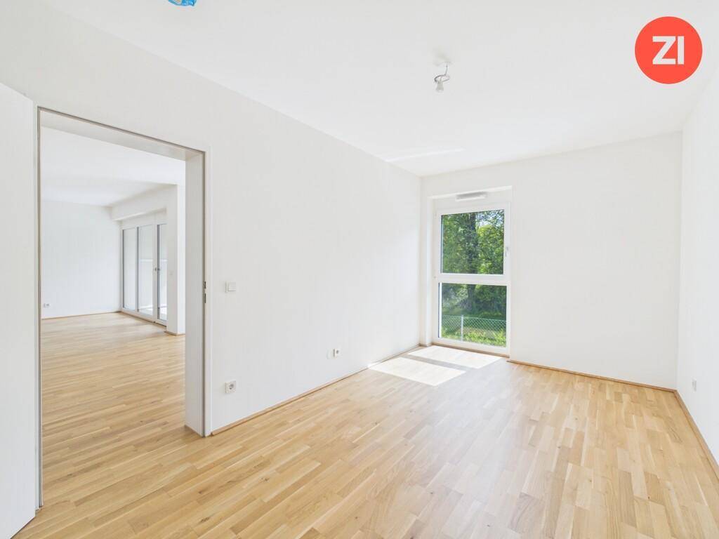 Helles Zimmer mit Parkettboden und einem Fenster mit Blick ins Grüne.
