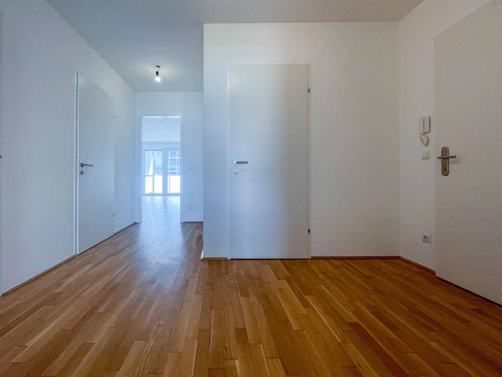 Langer, heller Flur mit Parkettboden und weißen Türen, der zu weiteren Räumen führt.