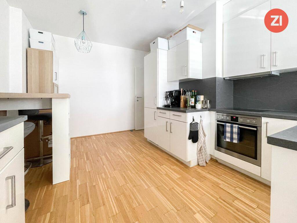 Moderne Küche mit weißen Schränken, dunkler Arbeitsplatte und Holzboden.