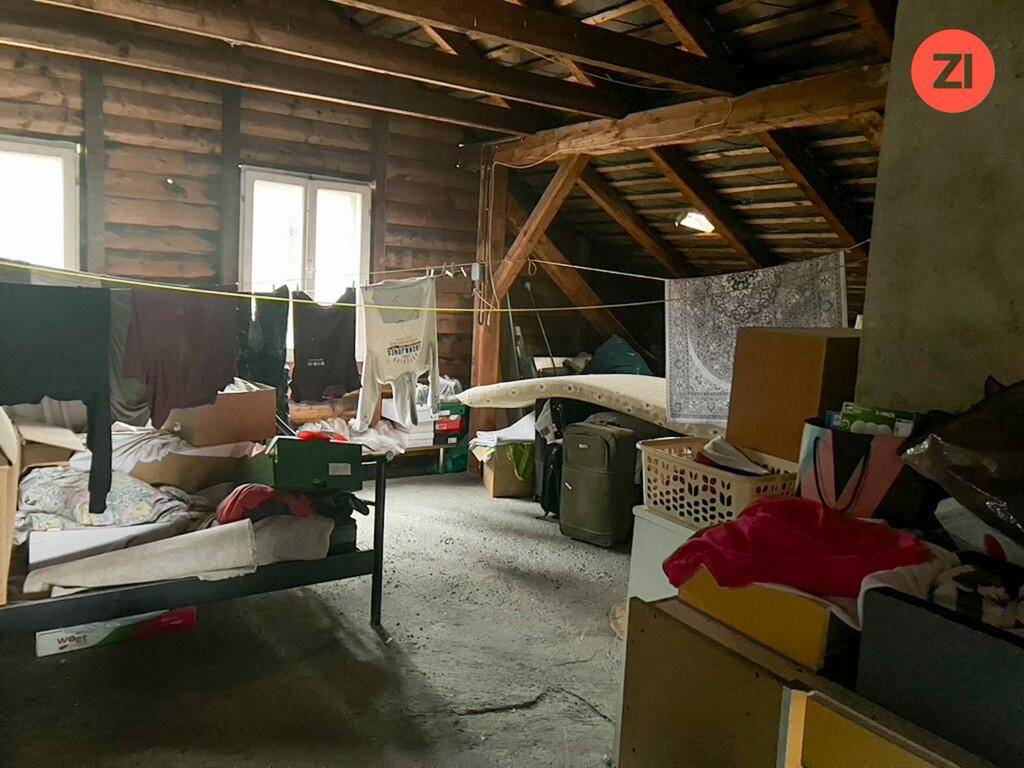 Dachboden mit sichtbarer Holzkonstruktion, Wäscheleinen und verschiedenen gelagerten Gegenständen.