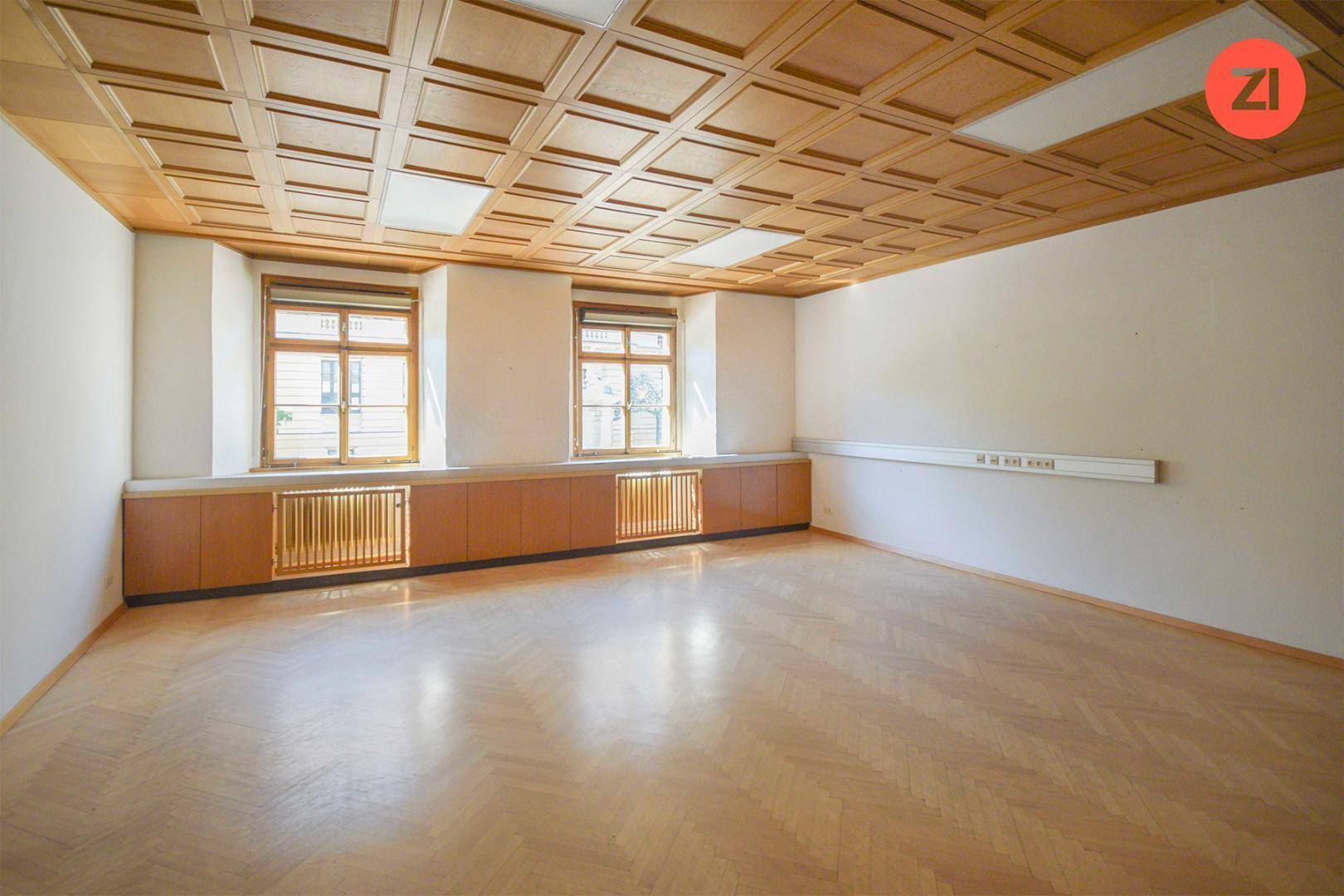 Geräumiges Büro mit Holzkassettendecke, zwei Fenstern und Fischgrätparkett, bietet eine klassische Atmosphäre.