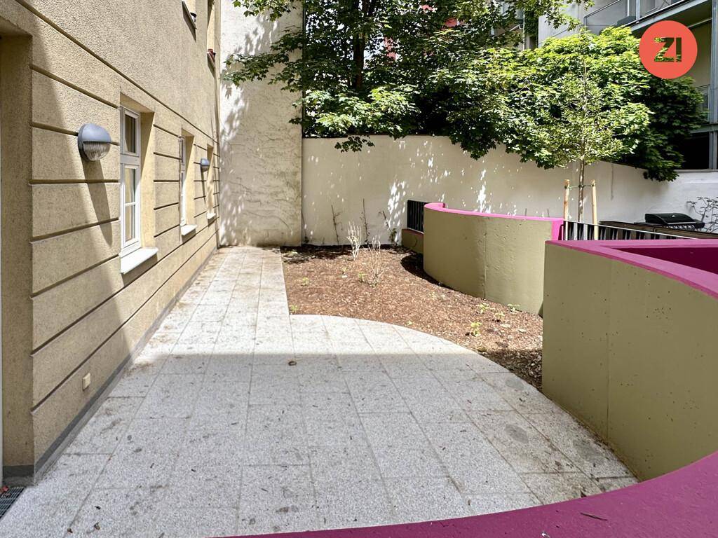 Gepflasterte Terrasse mit kleinen Grünflächen und modernen, farbigen Gestaltungselementen im Außenbereich.