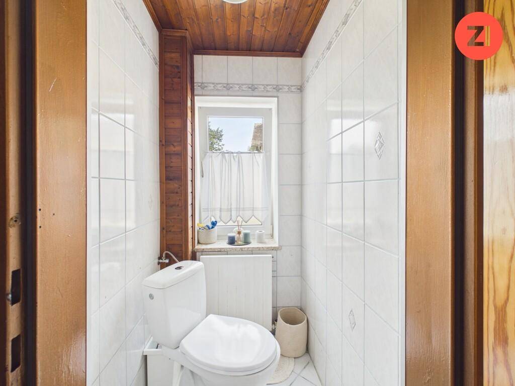 Kleines Gäste-WC mit Fenster, Holzdecke und weißen Wandfliesen.