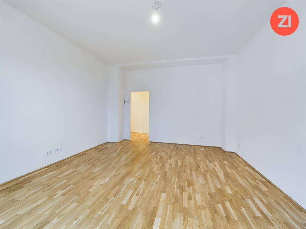 Geräumiger, heller Raum mit Holzboden und weiß gestrichenen Wänden, ideal für ein Wohnzimmer.