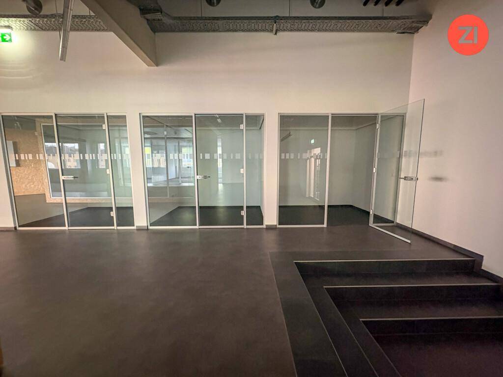 Moderner Bürogang mit Glaswänden zu einzelnen Büros und dunklem Bodenbelag.