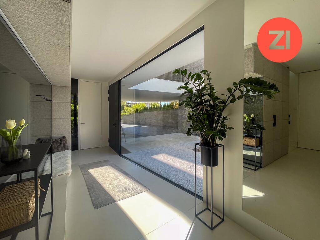 Heller Eingangsbereich mit großen Glasfronten und minimalistischer Dekoration, die zum Außenbereich führt.