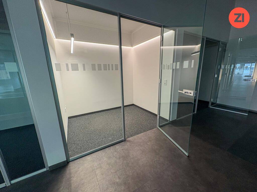 Kleiner, heller Büroraum mit Glaswänden, Teppichboden und moderner Beleuchtung.