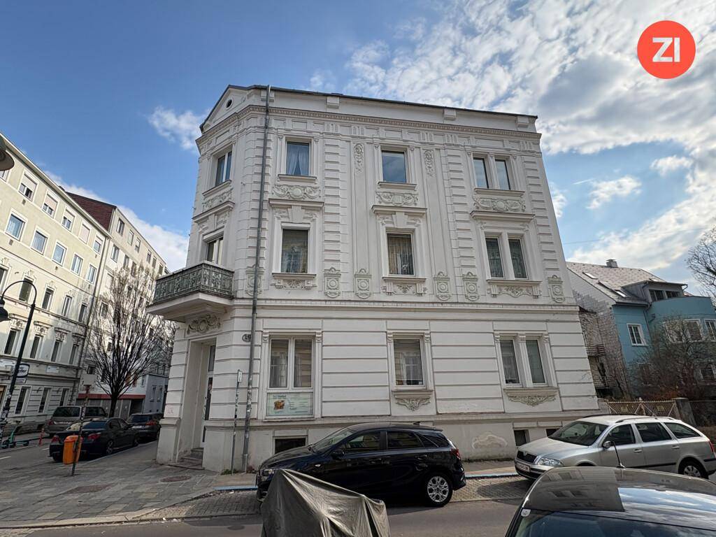 Historisches Eckhaus mit reich verzierter Fassade und kleinem Balkon unter blauem Himmel.