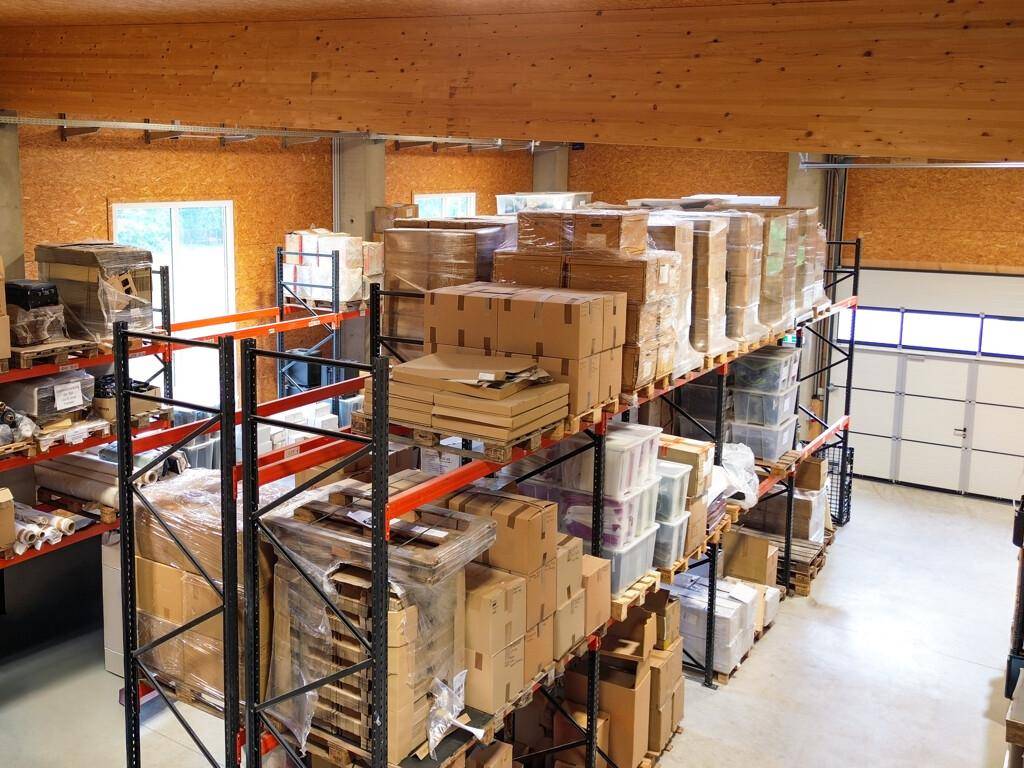 Blick in die Lagerhalle mit hohen Regalen, gefüllt mit Waren und einem großen Rolltor im Hintergrund.