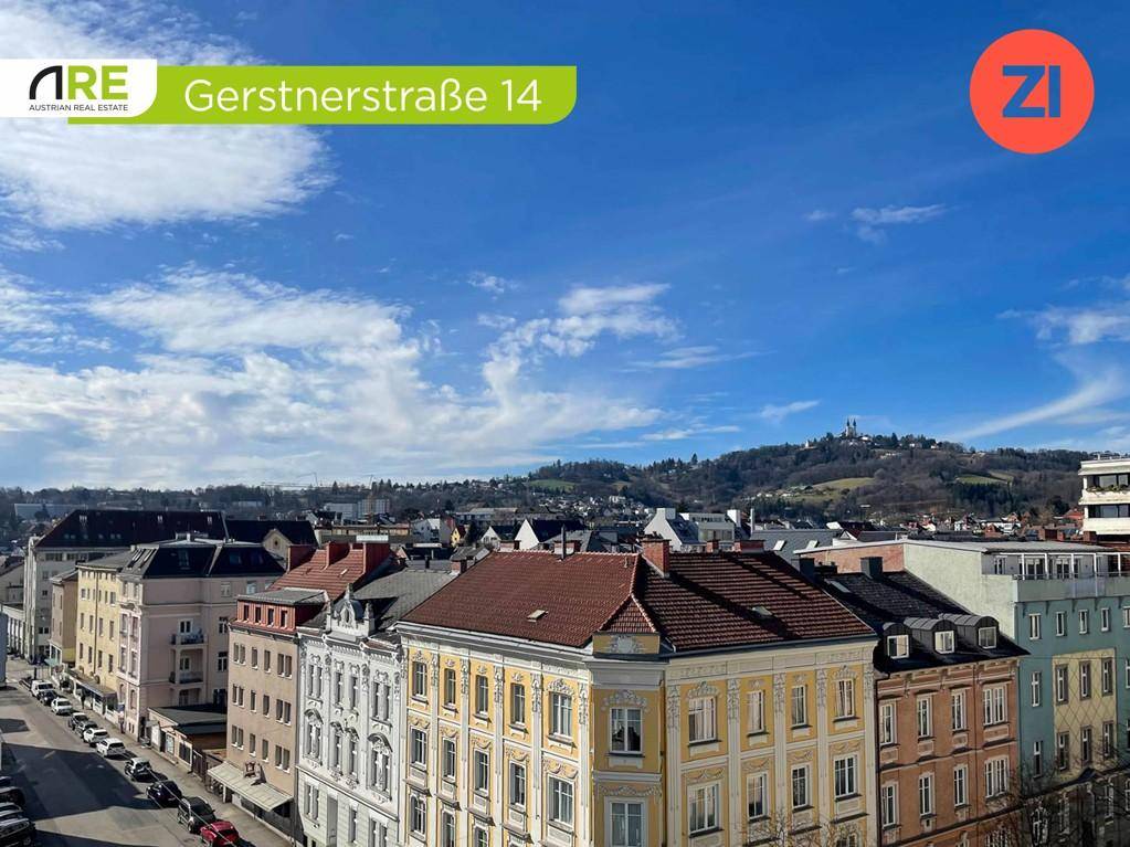 Panoramablick über eine Stadt mit vielen Dächern, Hügeln und einem markanten Gebäude in der Ferne.