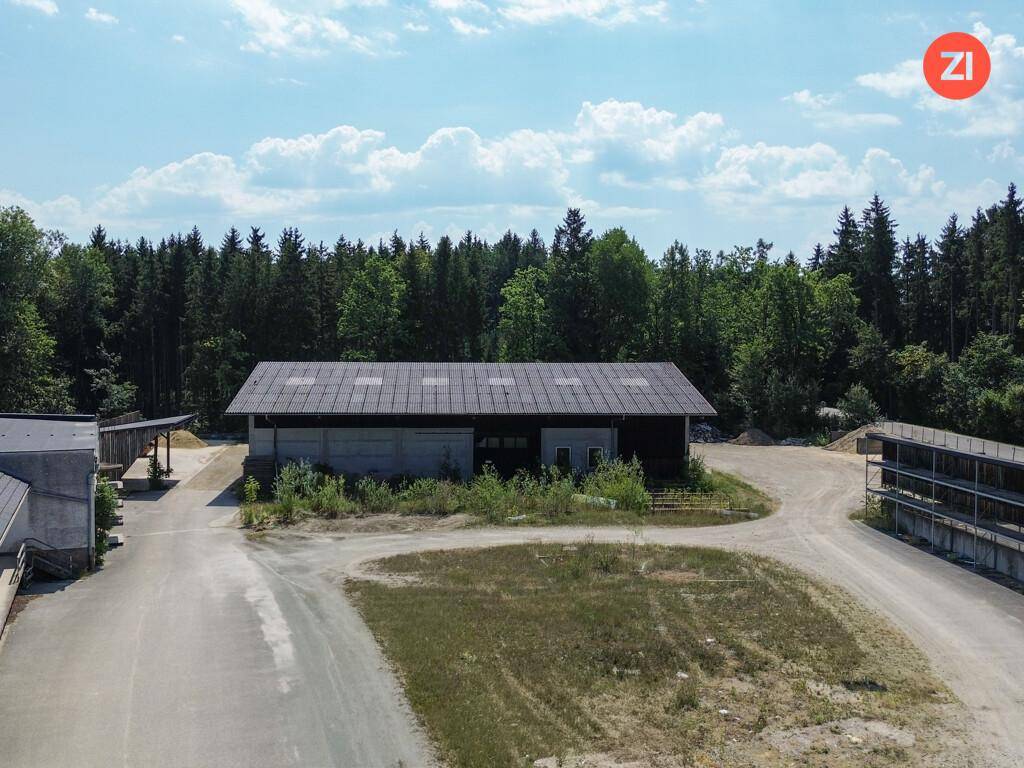 Großes Lagergebäude mit dunklem Dach und Betonwänden, umgeben von einer weitläufigen Freifläche und Wald.