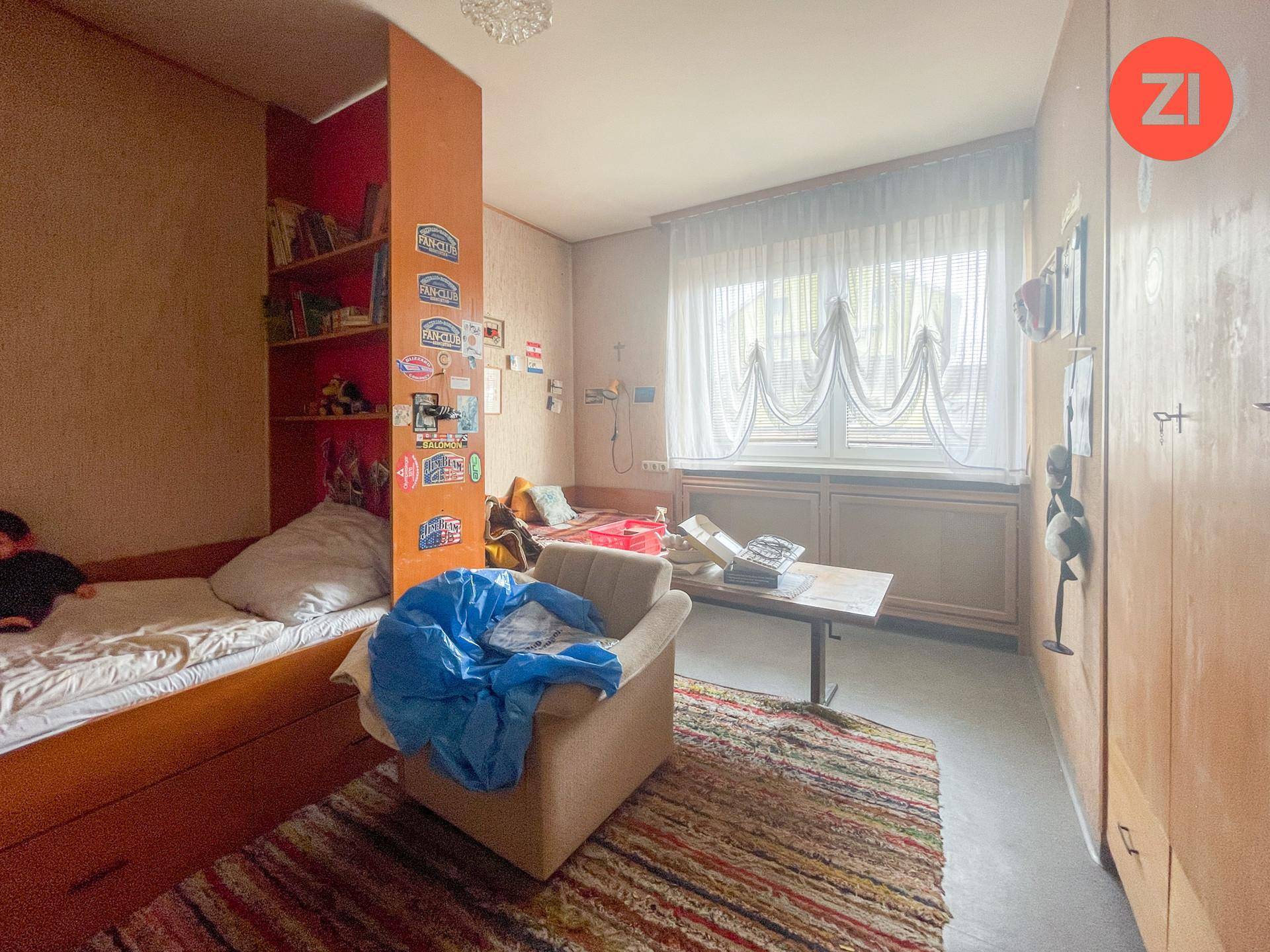 Kinder- oder Gästezimmer mit zwei Betten, Holzmöbeln und farbenfroher Dekoration, hell durch ein Fenster.
