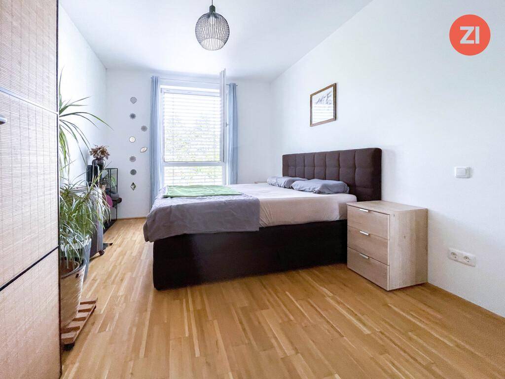 Helles Schlafzimmer mit Holzboden, Doppelbett und großem Fenster.