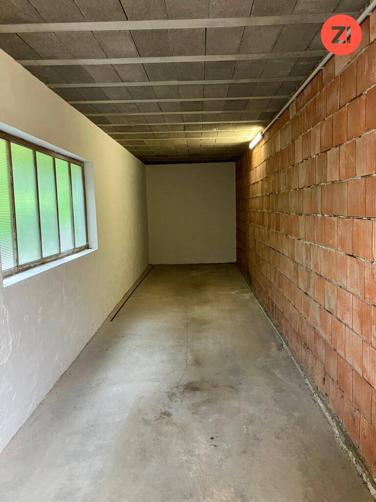 Langer, schmaler Raum mit unverputzten Ziegelwänden und einem Fenster, ideal als Abstellraum.