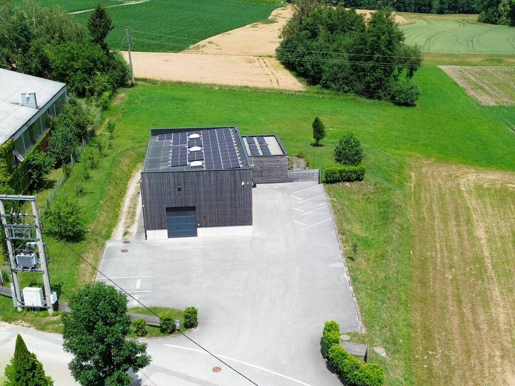 Luftaufnahme des Gebäudes von hinten mit großem Parkplatz und angrenzenden Feldern unter blauem Himmel.