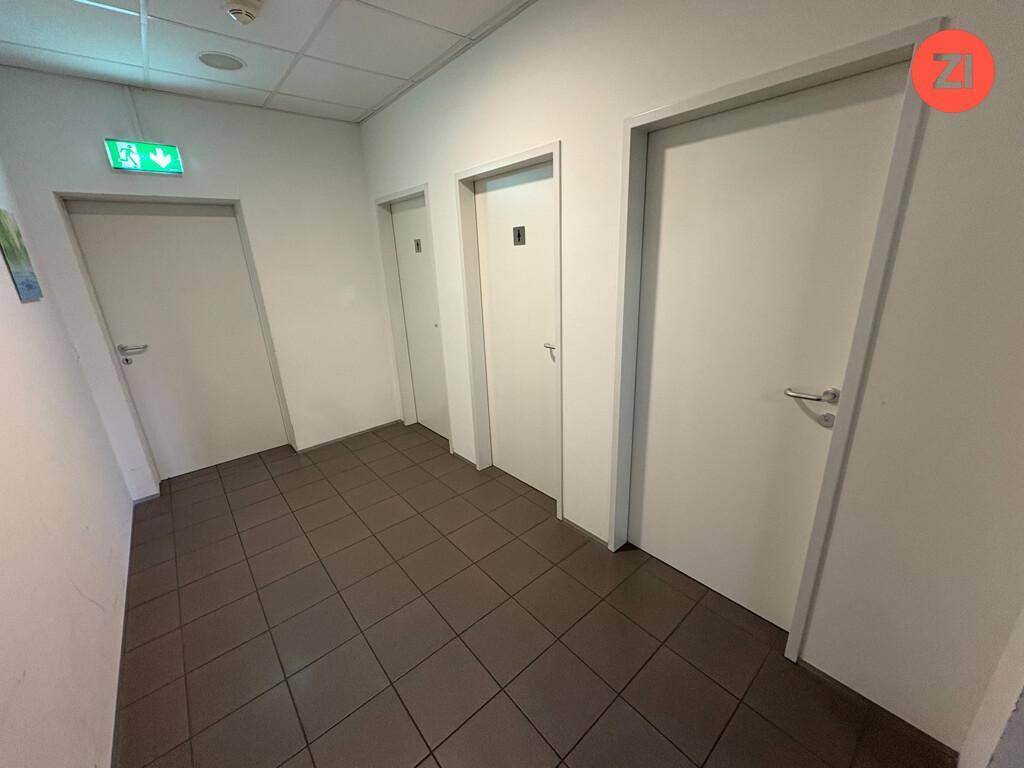 Schlichter Flur mit mehreren Türen und dunklem Fliesenboden, beleuchtet von einer Notausgangsleuchte.