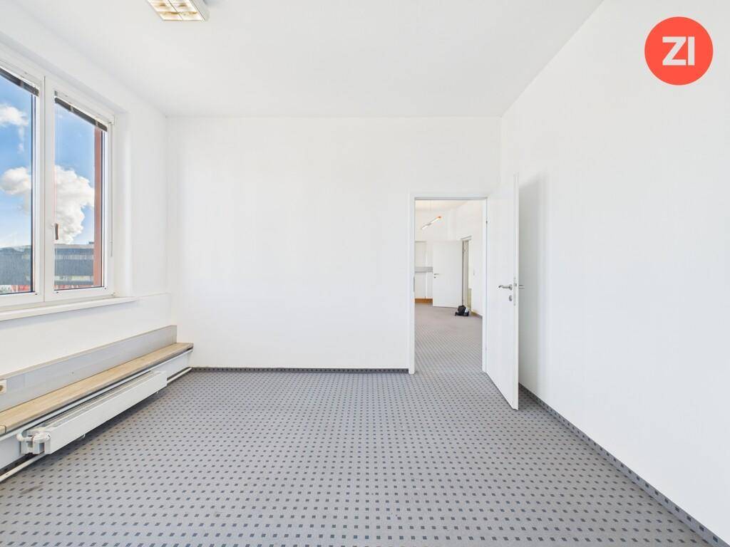 Helles, leeres Büro mit Teppichboden, weißen Wänden und Blick auf den Himmel durch das Fenster.