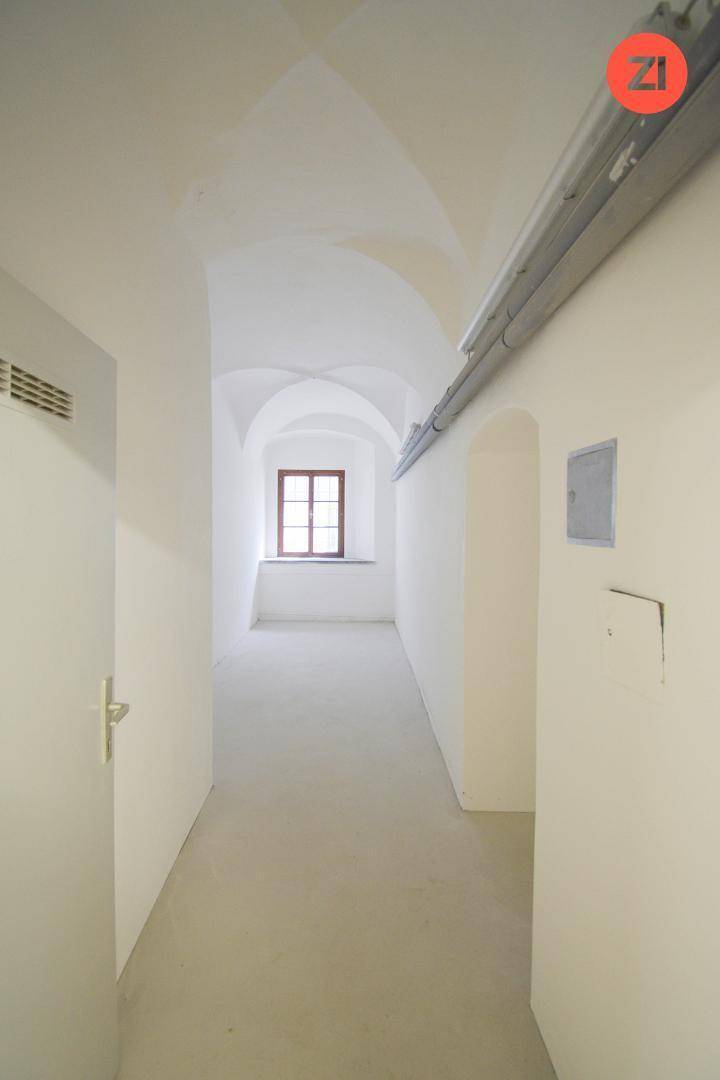 Langer Flur mit gewölbter Decke, Fenster am Ende und einfacher Ausstattung, verbindet verschiedene Bereiche.