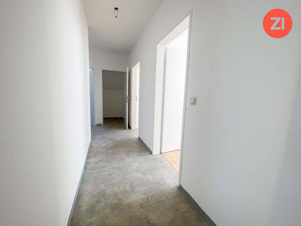 Heller Flur mit Betonboden und weißen Wänden, der zu weiteren Räumen führt.