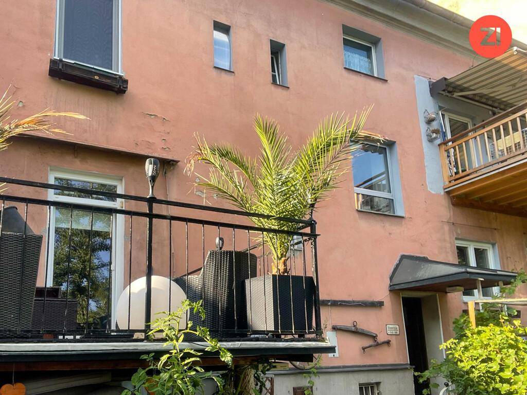Kleiner Balkon mit Palme und Sitzgelegenheiten an der rosafarbenen Fassade des Gebäudes.