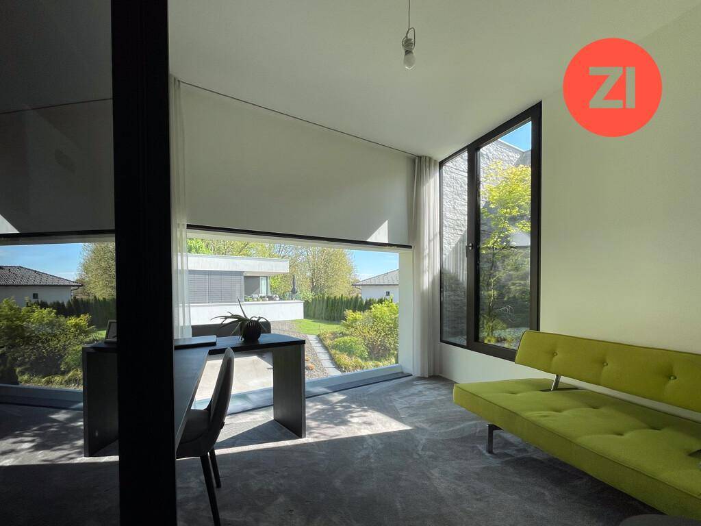 Helles Arbeitszimmer mit großen Fenstern, Blick ins Grüne und modernem Sofa.