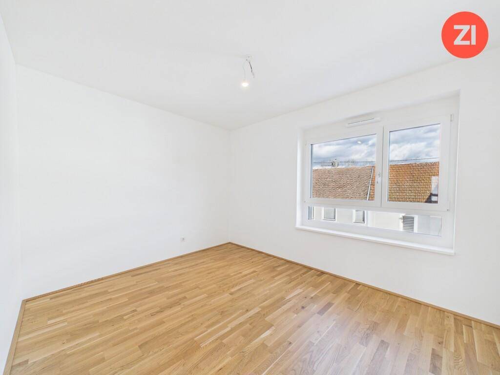 Ruhiges Schlafzimmer mit hellem Parkettboden und Blick auf die umliegenden Dächer.