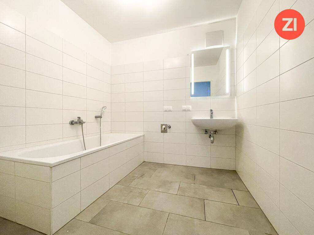 Modern gefliestes Badezimmer mit Badewanne, Waschbecken und beleuchtetem Spiegelschrank.