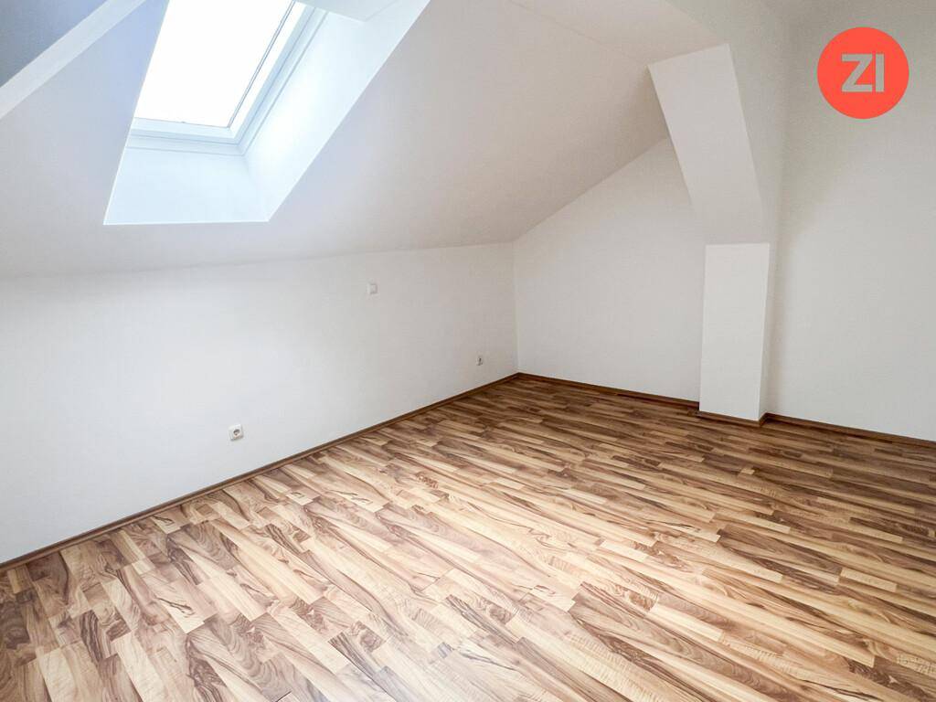 Helles Dachzimmer mit Laminatboden, Dachfenster und schrägen Wänden für gemütliches Wohnen.