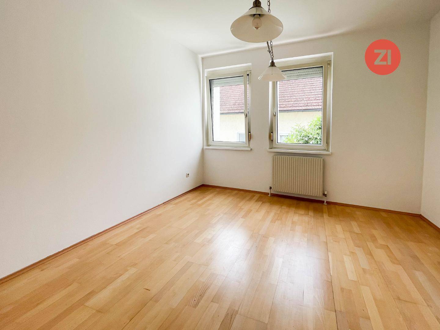 Helles Schlafzimmer mit Holzboden und zwei Fenstern, die viel Tageslicht hereinlassen.