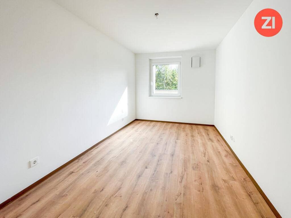 Unmöbliertes Zimmer mit Laminatboden und einem Fenster, das eine grüne Aussicht bietet.