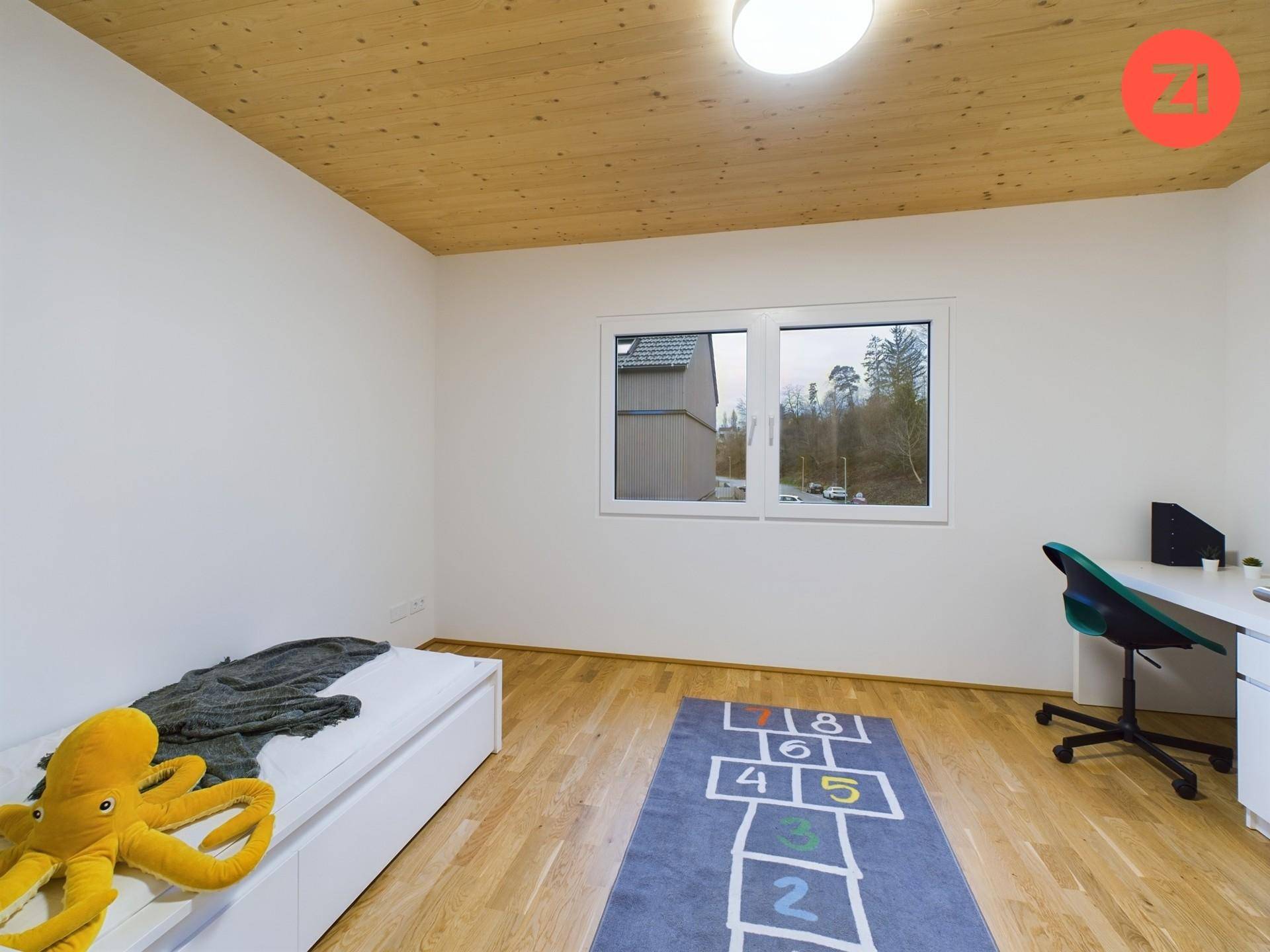 Kinderzimmer mit Holzboden, großem Fenster und Blick ins Grüne.