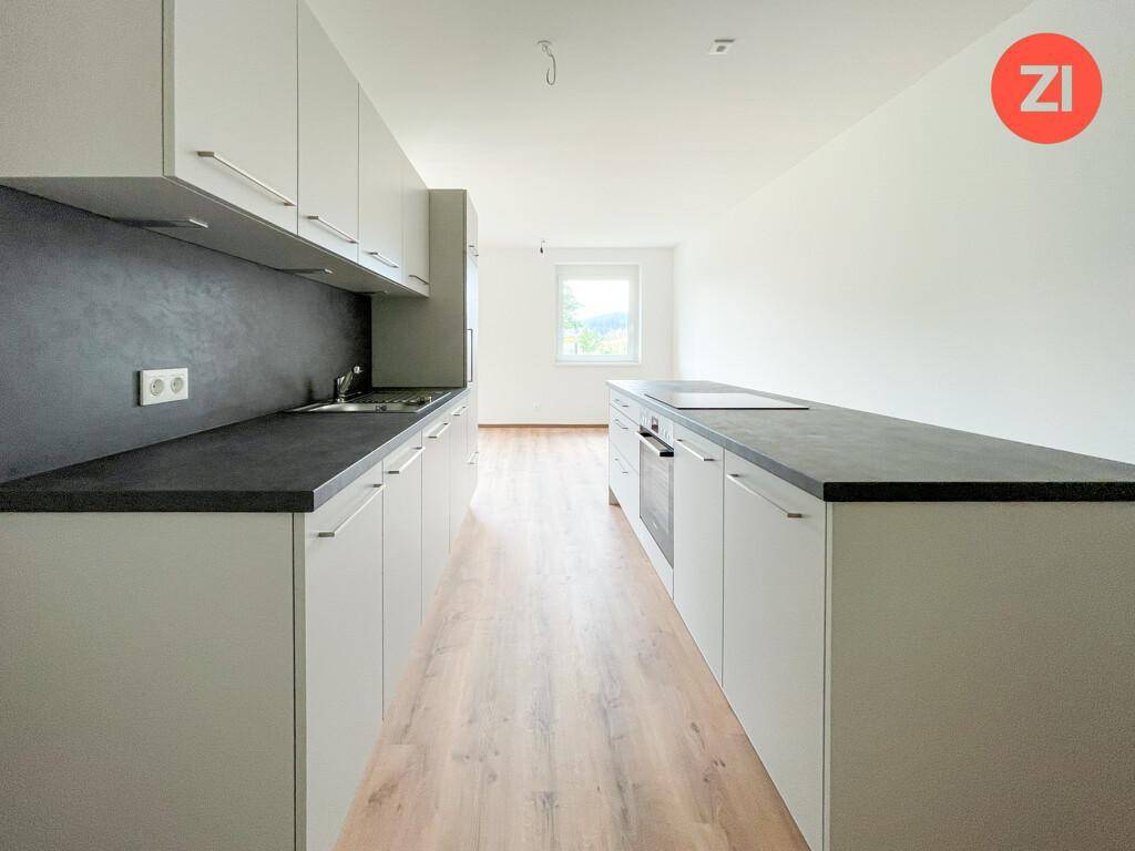 Helle, moderne Küche mit Küchenzeile, Insel und Blick ins Grüne durch das Fenster.