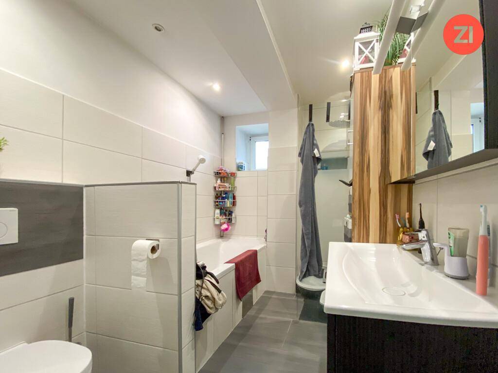 Modernes Badezimmer mit Badewanne, Dusche, weißen Fliesen und einem Fenster für natürliches Licht.