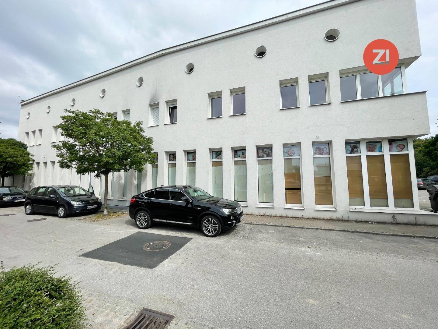 Außenansicht eines weißen Gebäudes mit geparkten Autos davor, das eine moderne Architektur aufweist.