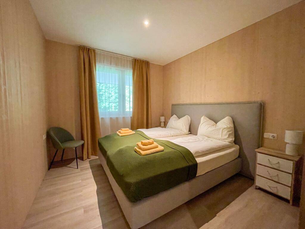 Gemütliches Schlafzimmer mit Doppelbett, Holzwand und Blick ins Grüne durch das Fenster.